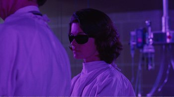 Movie still from “Coma” (1978), directed by Michael Crichton – A woman wearing sunglasses standing in a purple room; Medium shot, Low angle