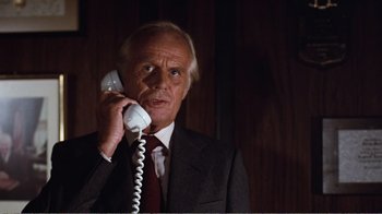 Movie still from “Coma” (1978), directed by Michael Crichton – An older man wearing a suit and tie talking on a phone; Close Up shot, Low angle