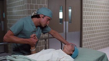 Movie still from “Coma” (1978), directed by Michael Crichton – A man wearing a surgical gown and a hat is standing over a patient; Close Up shot, Low angle