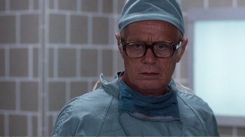 Movie still from “Coma” (1978), directed by Michael Crichton – A man wearing a surgical mask and a surgical gown; Close Up shot, Low angle