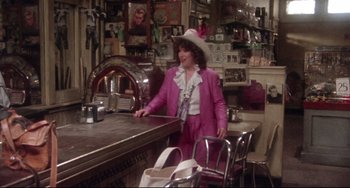 Movie still from “Come Back to the 5 & Dime Jimmy Dean, Jimmy Dean” (1982), directed by Robert Altman – A woman wearing a pink suit and a white hat standing at a counter; Wide shot, High angle