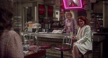 Movie still from “Come Back to the 5 & Dime Jimmy Dean, Jimmy Dean” (1982), directed by Robert Altman – Two women sitting at a counter in front of a neon sign; Wide shot, High angle