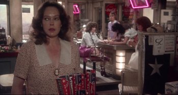Movie still from “Come Back to the 5 & Dime Jimmy Dean, Jimmy Dean” (1982), directed by Robert Altman – A woman holding a bag in front of a group of people in a bar; Medium shot, Over the shoulder angle