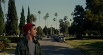 Movie still from “Comet” (2014), directed by Sam Esmail – A young man wearing a red hat standing on the side of a road; Medium shot, Low angle