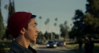 Movie still from “Comet” (2014), directed by Sam Esmail – A young man wearing a red hat standing in front of a street; Close Up shot, Low angle