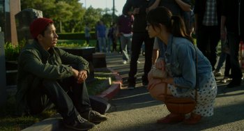 Movie still from “Comet” (2014), directed by Sam Esmail – A woman kneeling down next to a man on the street; Medium shot, Over the shoulder angle