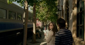 Movie still from “Comet” (2014), directed by Sam Esmail – A woman standing on the side of the street holding a book; Wide shot, Over the shoulder angle