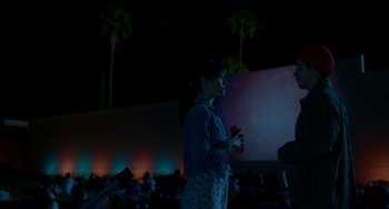 Movie still from “Comet” (2014), directed by Sam Esmail – A woman standing in front of an audience at night; Medium shot, Over the shoulder angle