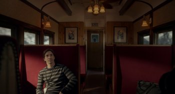 Movie still from “Comet” (2014), directed by Sam Esmail – A man sitting on a train seat in a train car; Medium shot, High angle