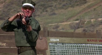 Movie still from “Coming Home” (1978), directed by Hal Ashby – A man holding a rifle in front of a sign; Medium shot, Over the shoulder angle