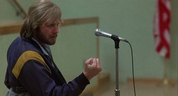 Movie still from “Coming Home” (1978), directed by Hal Ashby – A man with long blond hair is speaking at a microphone; Medium shot, Low angle