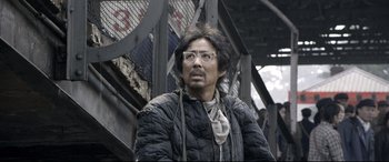 Movie still from “Coming Home” (2014), directed by Yimou Zhang – A man wearing glasses and a black jacket; Close Up shot, Low angle