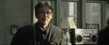 Movie still from “Coming Home” (2014), directed by Yimou Zhang – A man with glasses is sitting in front of a lamp; Close Up shot, Over the shoulder angle