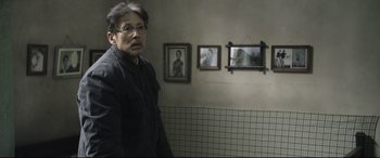 Movie still from “Coming Home” (2014), directed by Yimou Zhang – A man standing next to a wall in front of three framed pictures; Medium shot, Over the shoulder angle