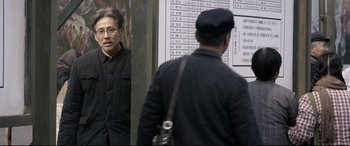 Movie still from “Coming Home” (2014), directed by Yimou Zhang – A man standing in front of another man in front of a sign; Medium shot, Over the shoulder angle