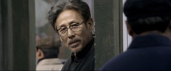 Movie still from “Coming Home” (2014), directed by Yimou Zhang – An older man wearing glasses and a black shirt; Close Up shot, Over the shoulder angle