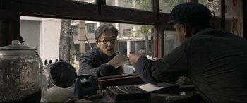 Movie still from “Coming Home” (2014), directed by Yimou Zhang – A man sitting in front of another man holding a piece of paper; Medium shot, Over the shoulder angle