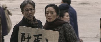 Movie still from “Coming Home” (2014), directed by Yimou Zhang – An asian woman holding a sign in front of a crowd; Close Up shot, High angle