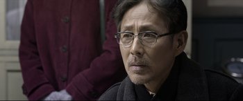 Movie still from “Coming Home” (2014), directed by Yimou Zhang – An older man wearing glasses and a black jacket; Close Up shot, Over the shoulder angle