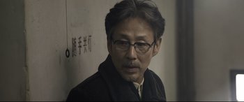 Movie still from “Coming Home” (2014), directed by Yimou Zhang – A person wearing glasses and a jacket; Close Up shot, Over the shoulder angle