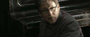 Movie still from “Coming Home” (2014), directed by Yimou Zhang – A person wearing glasses sitting on steps; Close Up shot, Over the shoulder angle
