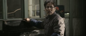 Movie still from “Coming Home” (2014), directed by Yimou Zhang – An asian man in glasses is leaning against a counter; Medium shot, Over the shoulder angle