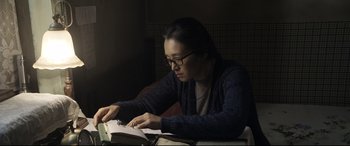 Movie still from “Coming Home” (2014), directed by Yimou Zhang – A woman sitting at a table reading a book; Medium shot, High angle
