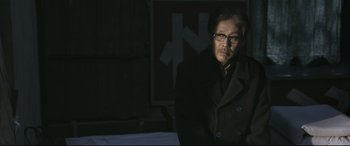 Movie still from “Coming Home” (2014), directed by Yimou Zhang – A man wearing glasses and a coat standing in the dark; Medium shot, Over the shoulder angle