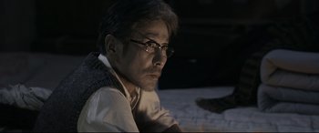 Movie still from “Coming Home” (2014), directed by Yimou Zhang – A man wearing glasses sitting on the ground; Close Up shot, Over the shoulder angle