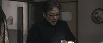 Movie still from “Coming Home” (2014), directed by Yimou Zhang – An older man wearing glasses looking down at a piece of paper; Close Up shot, Over the shoulder angle