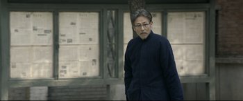 Movie still from “Coming Home” (2014), directed by Yimou Zhang – A man standing in front of a building with his hands in his pockets; Medium shot, Low angle