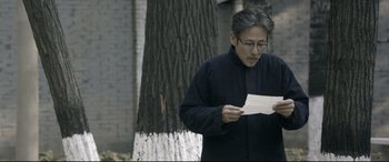 Movie still from “Coming Home” (2014), directed by Yimou Zhang – An older man reading a piece of paper in front of a tree; Medium shot, Over the shoulder angle