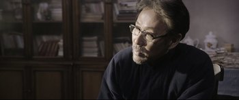 Movie still from “Coming Home” (2014), directed by Yimou Zhang – An older man wearing glasses and sitting in front of a bookshelf; Close Up shot, Over the shoulder angle