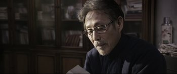 Movie still from “Coming Home” (2014), directed by Yimou Zhang – A man with glasses is looking down at a piece of paper; Close Up shot, Low angle
