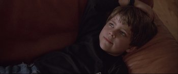 Movie still from “Communion” (1989), directed by Philippe Mora – A boy laying on a couch looking up at the camera; Close Up shot, Low angle