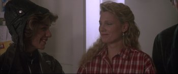 Movie still from “Communion” (1989), directed by Philippe Mora – A woman in a plaid shirt is smiling at the camera; Close Up shot, Over the shoulder angle