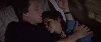 Movie still from “Communion” (1989), directed by Philippe Mora – A man and a boy laying in bed together; Close Up shot, Low angle