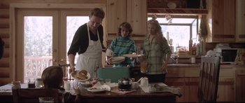 Movie still from “Communion” (1989), directed by Philippe Mora – A group of people standing around a table with food; Medium shot, Over the shoulder angle