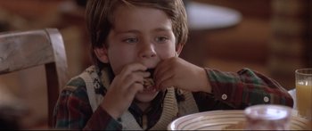 Movie still from “Communion” (1989), directed by Philippe Mora – A young boy is eating a sandwich at a table; Close Up shot, High angle