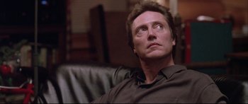 Movie still from “Communion” (1989), directed by Philippe Mora – A person sitting on a couch; Close Up shot, Low angle