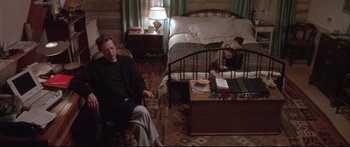 Movie still from “Communion” (1989), directed by Philippe Mora – A man and a woman sitting on a chair in a bedroom; Wide shot, High angle