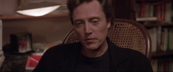 Movie still from “Communion” (1989), directed by Philippe Mora – A person sitting in a chair wearing a black shirt; Close Up shot, Low angle