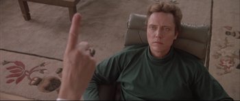 Movie still from “Communion” (1989), directed by Philippe Mora – A man sitting in a chair holding a finger up; Close Up shot, Over the shoulder angle