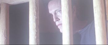 Movie still from “Communion” (1989), directed by Philippe Mora – A person looking through a fence; Close Up shot, Low angle