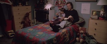Movie still from “Communion” (1989), directed by Philippe Mora – A woman and two children are sitting on a bed reading; Medium shot, High angle
