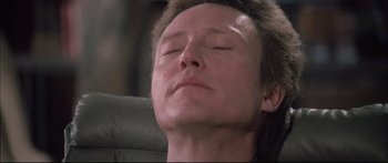 Movie still from “Communion” (1989), directed by Philippe Mora – A man with his eyes closed is sitting in an office chair; Close Up shot, Low angle