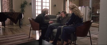 Movie still from “Communion” (1989), directed by Philippe Mora – A group of people sitting around a living room talking; Wide shot, High angle