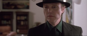 Movie still from “Communion” (1989), directed by Philippe Mora – A man wearing a hat and a green shirt; Close Up shot, Low angle