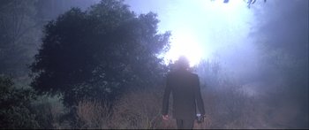 Movie still from “Communion” (1989), directed by Philippe Mora – A man in a black suit is walking through a field; Wide shot, Low angle