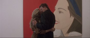 Movie still from “Communion” (1989), directed by Philippe Mora – A man and a woman embracing in front of a painting; Medium shot, Low angle